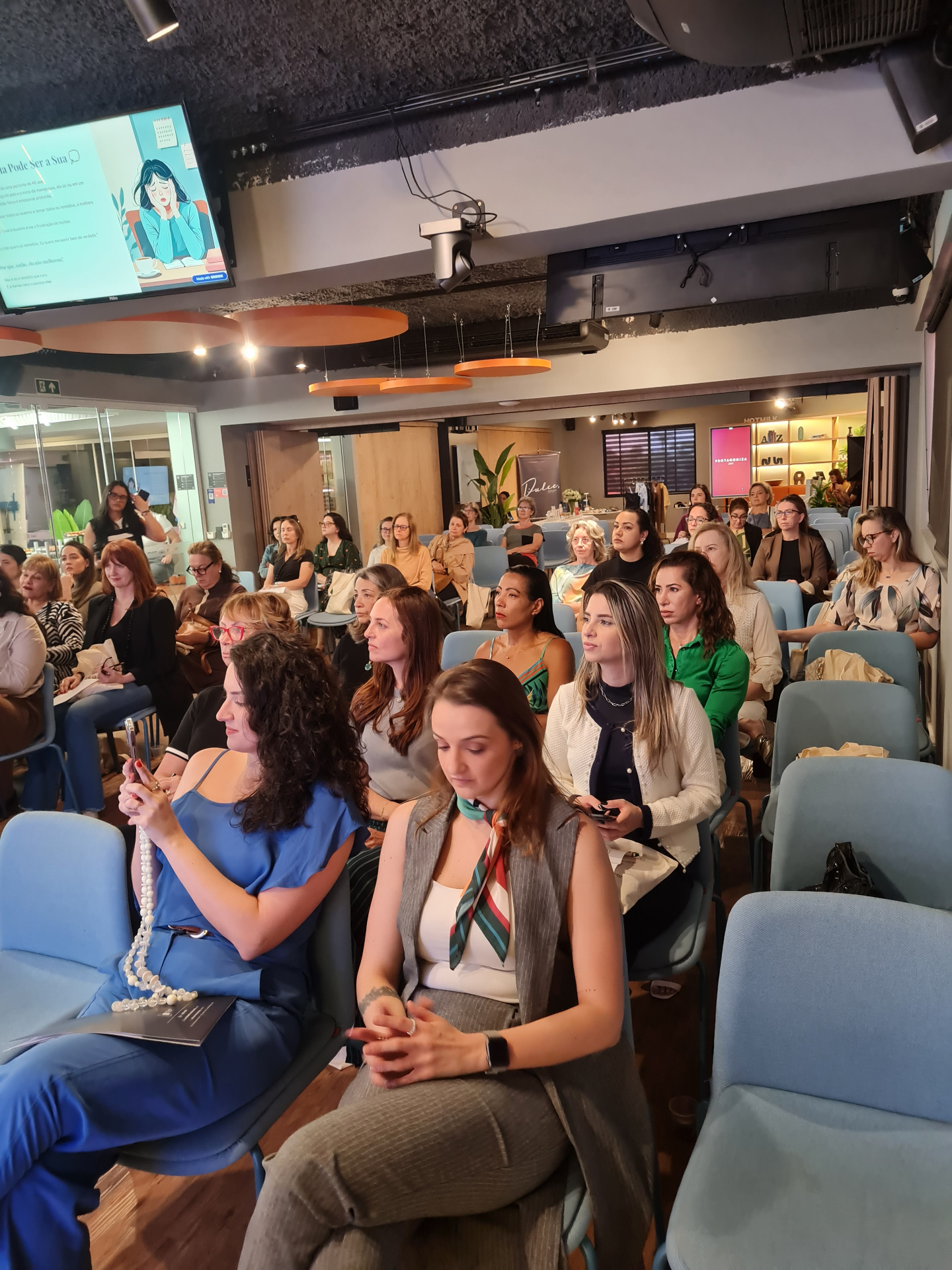 Auditório com mulheres 40+ participando do PROTAGONIZA 2025, atentas e sorridentes.