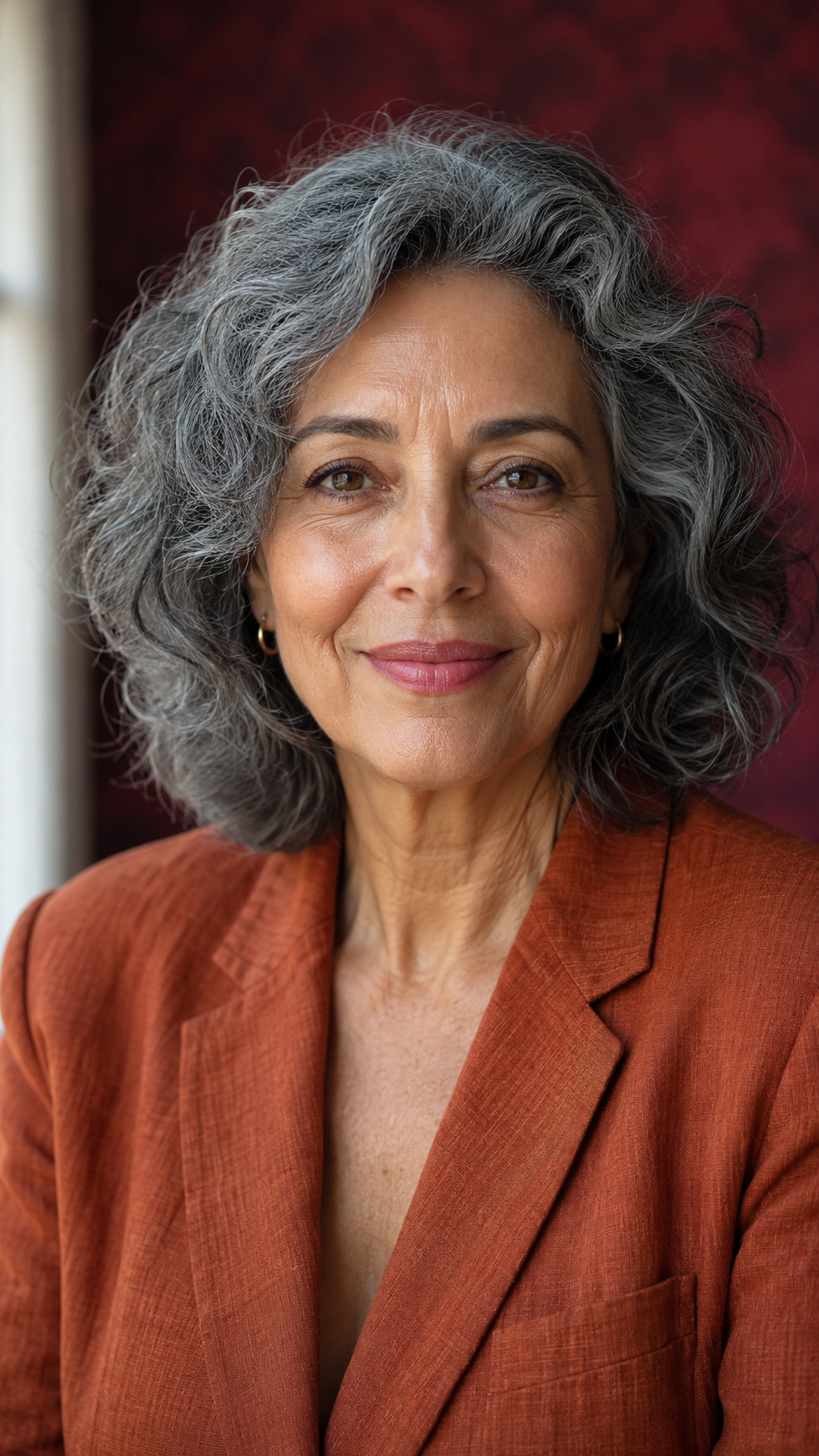 Retrato editorial de uma mulher 40+ com presença e serenidade, em frente a um fundo carmim.